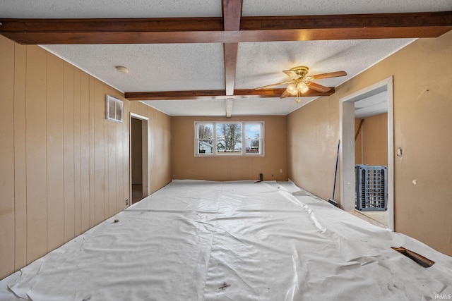 bedroom with a textured ceiling, beam ceiling, and wood walls