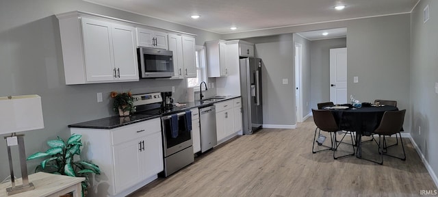 kitchen with appliances with stainless steel finishes, sink, white cabinets, dark stone counters, and light hardwood / wood-style floors