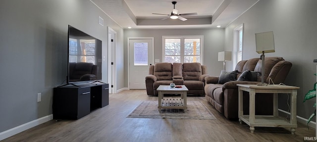 living room with a tray ceiling, light hardwood / wood-style floors, and ceiling fan