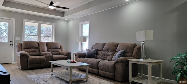 living room featuring light hardwood / wood-style flooring, ceiling fan, and a tray ceiling