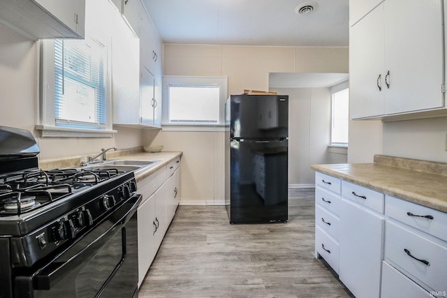 kitchen featuring sink, white cabinets, light wood-type flooring, and black appliances