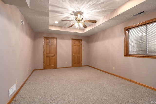 spare room with ceiling fan, carpet flooring, a tray ceiling, and a textured ceiling