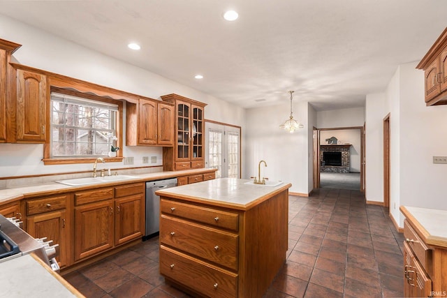 kitchen with sink, a brick fireplace, dishwasher, pendant lighting, and a kitchen island with sink