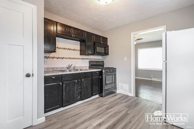 kitchen with dark brown cabinets, white fridge, gas stove, decorative backsplash, and light wood-type flooring