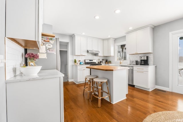 kitchen with wood counters, a breakfast bar, appliances with stainless steel finishes, hardwood / wood-style floors, and white cabinets