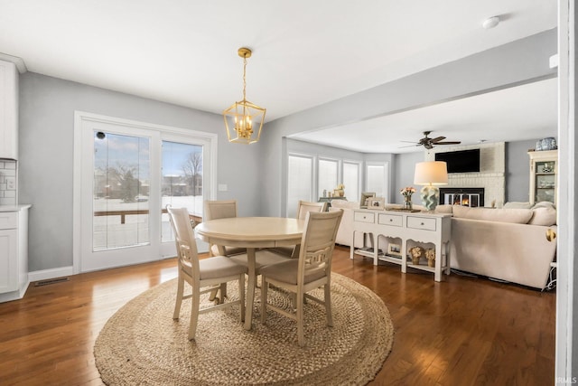 dining space featuring dark hardwood / wood-style flooring, ceiling fan with notable chandelier, and a brick fireplace