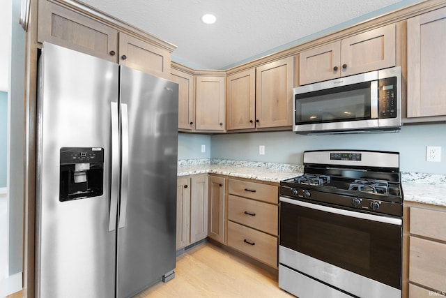 kitchen featuring appliances with stainless steel finishes, light stone countertops, light hardwood / wood-style floors, a textured ceiling, and light brown cabinetry