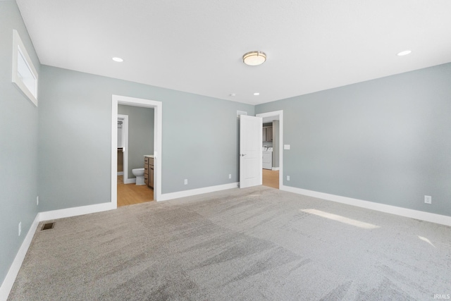 unfurnished bedroom with washer / dryer, light colored carpet, and ensuite bath