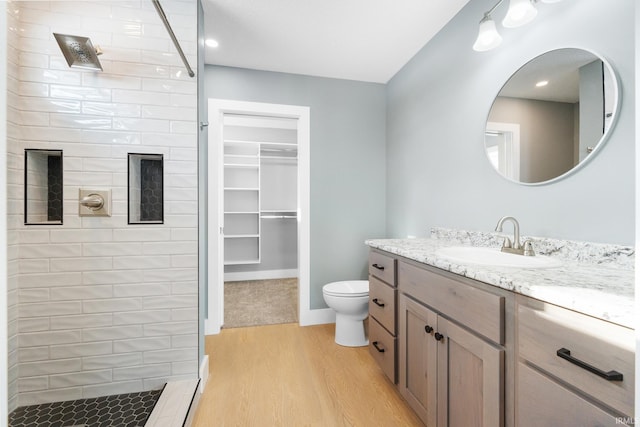 bathroom featuring wood-type flooring, a tile shower, vanity, and toilet