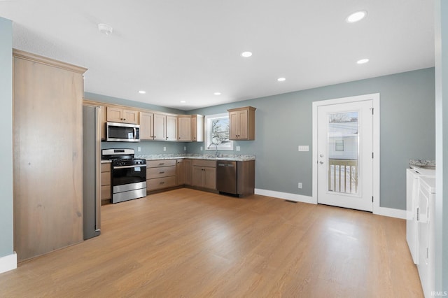 kitchen featuring appliances with stainless steel finishes, light brown cabinetry, sink, light stone counters, and light hardwood / wood-style floors