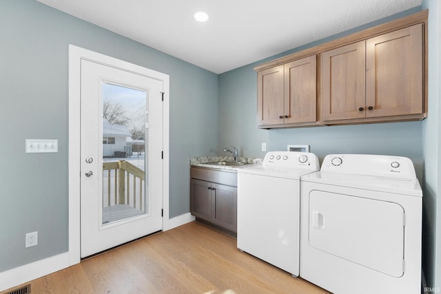 clothes washing area featuring sink, cabinets, washing machine and clothes dryer, and light wood-type flooring