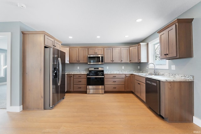 kitchen with stainless steel appliances, light stone countertops, sink, and light wood-type flooring