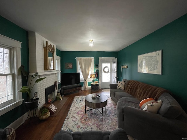 living room featuring a brick fireplace, wood-type flooring, and vaulted ceiling