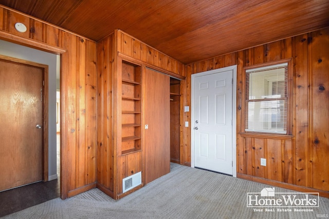 foyer entrance with wooden ceiling, carpet flooring, and wood walls