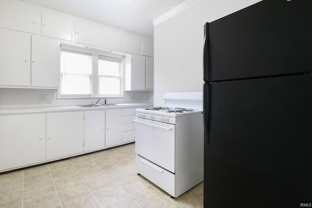 kitchen with sink, gas range gas stove, black fridge, crown molding, and white cabinets