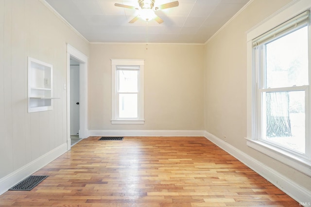 empty room with ornamental molding, built in shelves, ceiling fan, and light hardwood / wood-style flooring