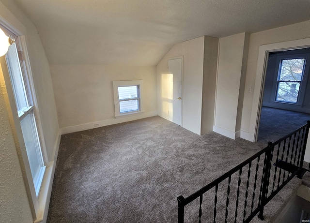 bonus room with dark colored carpet, lofted ceiling, a wealth of natural light, and a textured ceiling