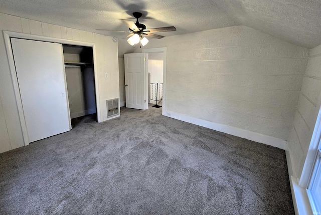 unfurnished bedroom with a closet, lofted ceiling, carpet, and a textured ceiling