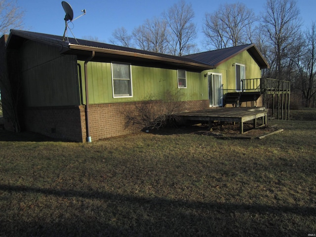 view of side of property with brick siding, a lawn, metal roof, and a deck