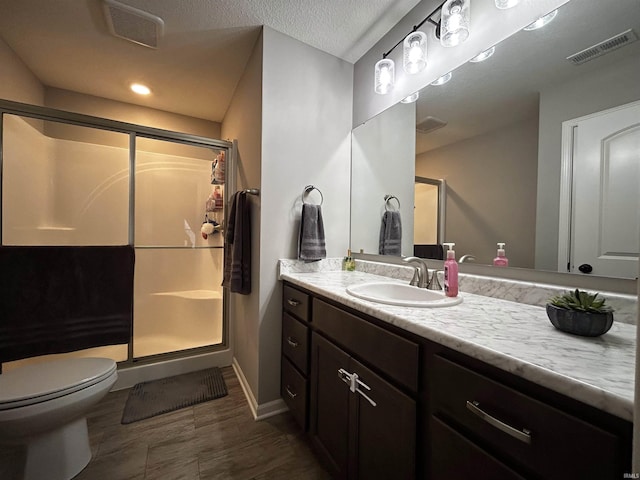 bathroom with vanity, a textured ceiling, a shower with shower door, and toilet