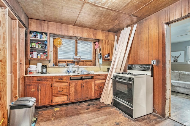 kitchen with sink, dark hardwood / wood-style floors, white gas range oven, and wood walls