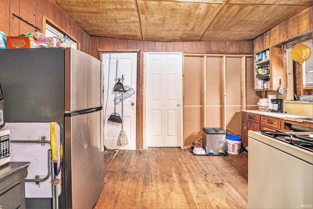 kitchen featuring light wood-type flooring, stainless steel refrigerator, white range with gas stovetop, and wood walls