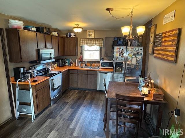 kitchen with appliances with stainless steel finishes, dark hardwood / wood-style floors, pendant lighting, sink, and dark brown cabinetry