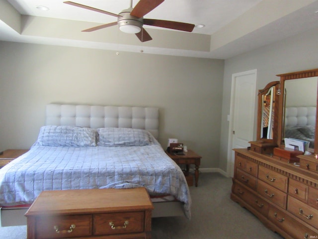 carpeted bedroom with ceiling fan and a tray ceiling