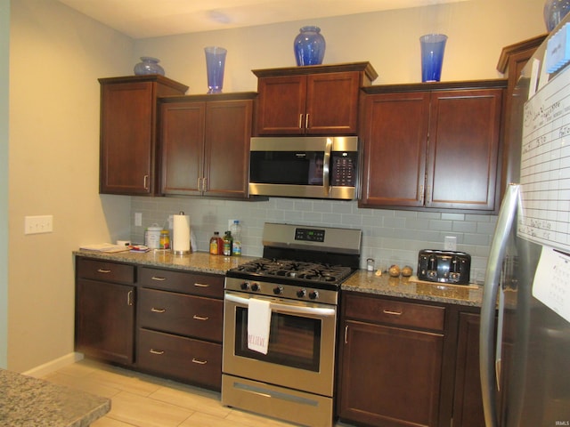 kitchen with appliances with stainless steel finishes, light tile patterned floors, decorative backsplash, and stone counters