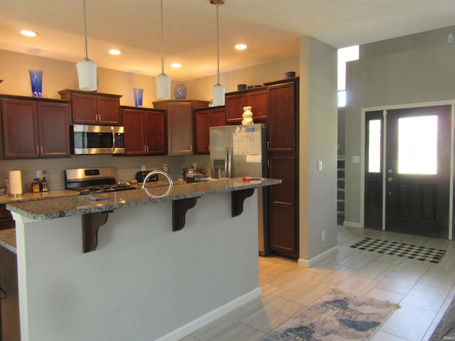 kitchen with a breakfast bar area, appliances with stainless steel finishes, dark stone countertops, a center island with sink, and decorative light fixtures