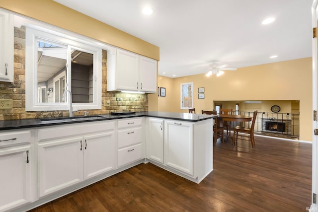 kitchen featuring sink, dark hardwood / wood-style floors, white cabinets, a brick fireplace, and kitchen peninsula