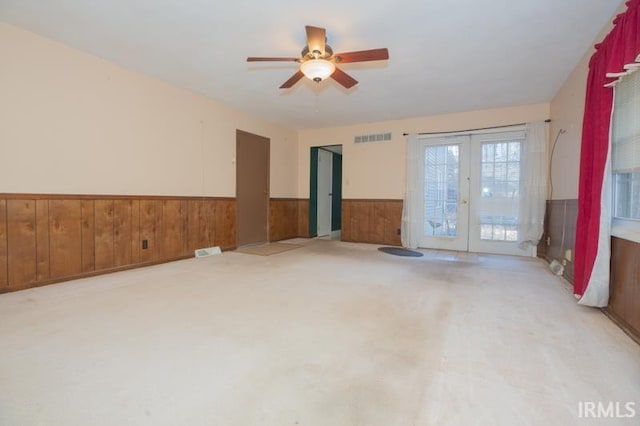 unfurnished room with french doors, ceiling fan, and wooden walls