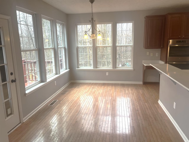 unfurnished dining area with a notable chandelier, a wealth of natural light, and light wood-type flooring