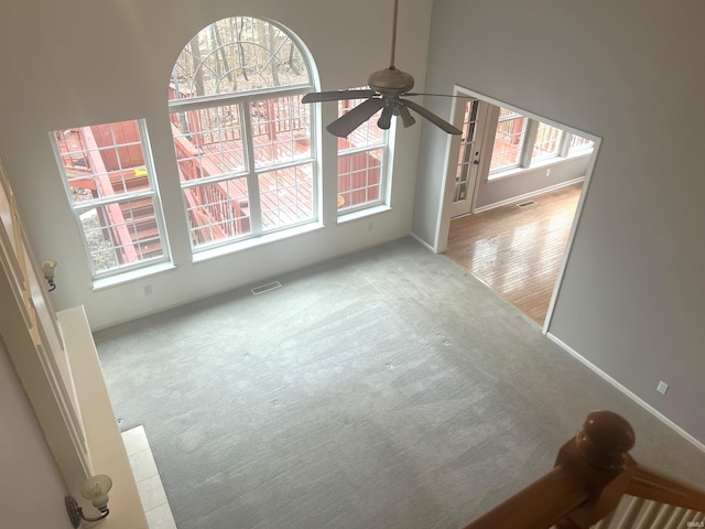 unfurnished living room with ceiling fan, carpet floors, and a wealth of natural light