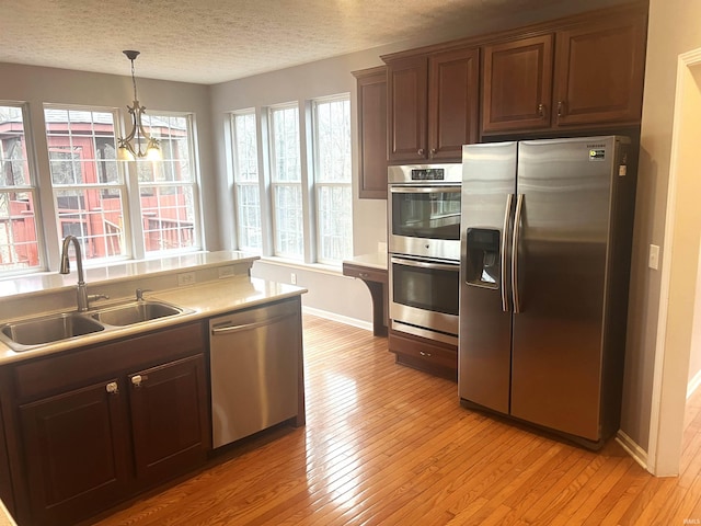 kitchen with sink, light hardwood / wood-style flooring, a textured ceiling, pendant lighting, and stainless steel appliances