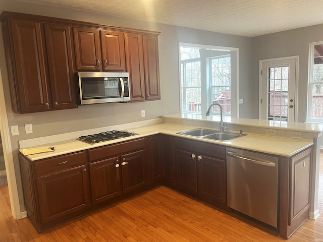 kitchen with sink, light wood-type flooring, kitchen peninsula, stainless steel appliances, and a textured ceiling