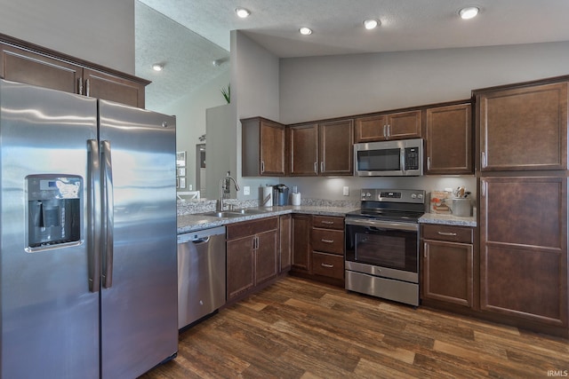 kitchen with appliances with stainless steel finishes, sink, dark hardwood / wood-style flooring, light stone countertops, and a textured ceiling