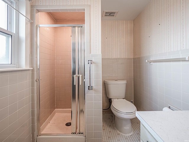 bathroom with a shower with shower door, tile walls, vanity, toilet, and tile patterned floors