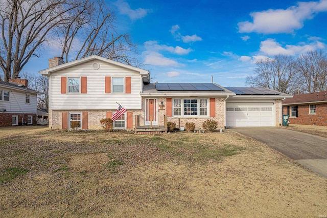 split level home featuring a garage, a front yard, and solar panels