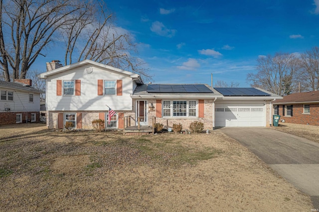 tri-level home featuring a garage, a front yard, and solar panels