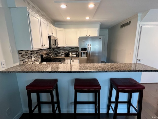 kitchen featuring a breakfast bar, white cabinetry, backsplash, kitchen peninsula, and stainless steel appliances