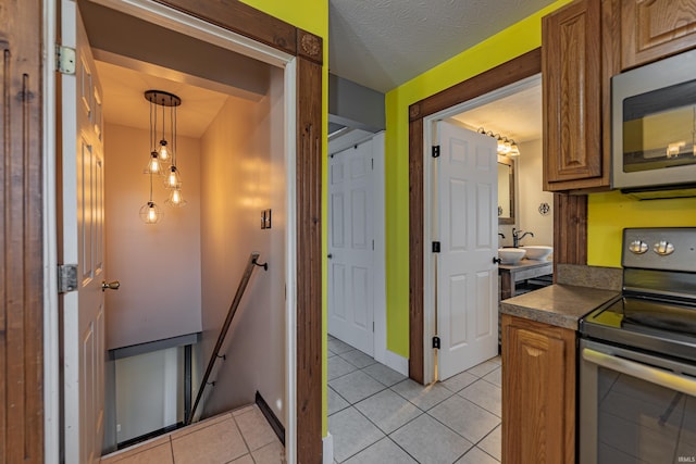 kitchen with appliances with stainless steel finishes, pendant lighting, a textured ceiling, and light tile patterned floors