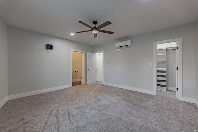 unfurnished bedroom with ceiling fan, a wall unit AC, ensuite bathroom, light carpet, and a walk in closet