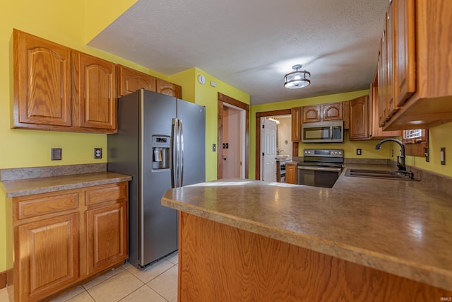 kitchen with sink, a textured ceiling, light tile patterned floors, appliances with stainless steel finishes, and kitchen peninsula