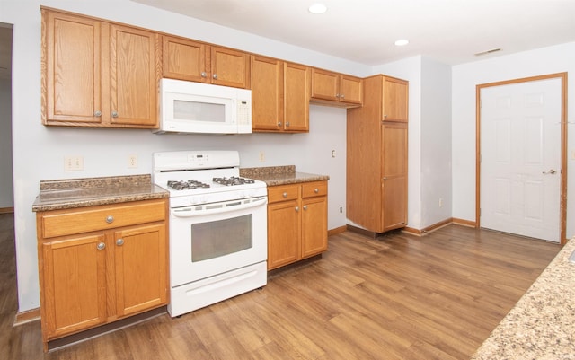 kitchen featuring white appliances, wood-type flooring, and stone counters