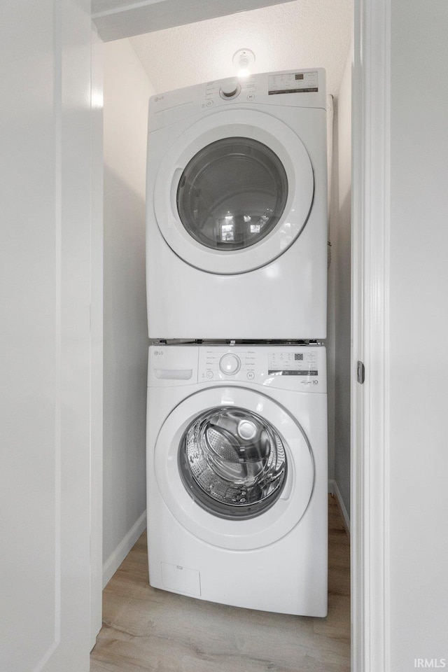 laundry area with stacked washing maching and dryer and light hardwood / wood-style floors