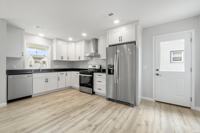 kitchen with wall chimney exhaust hood, sink, light hardwood / wood-style flooring, appliances with stainless steel finishes, and white cabinets