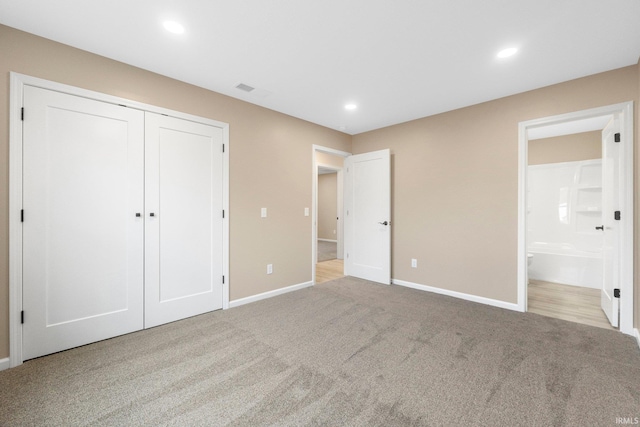 unfurnished bedroom with light colored carpet, a closet, and ensuite bath