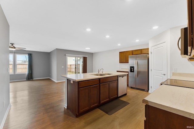 kitchen with sink, a kitchen island with sink, ceiling fan, stainless steel appliances, and light hardwood / wood-style floors