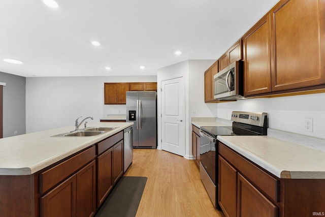 kitchen with appliances with stainless steel finishes, sink, an island with sink, and light wood-type flooring